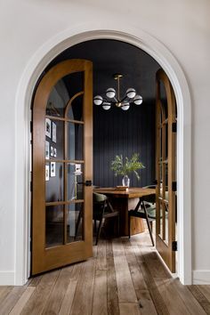 an arched doorway leads to a dining room with wood floors and black walls, along with a wooden table set for four