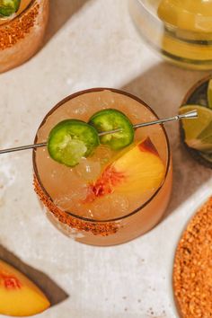 two glasses filled with drinks and garnishes on top of a white table