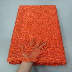 an orange lace with sequins on it is being held by a person's hand