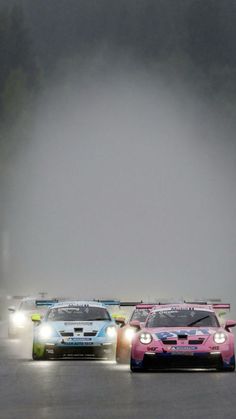 three cars driving on a race track with fog in the air behind them and trees