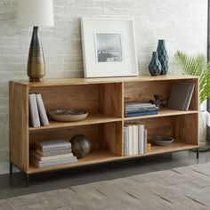 a wooden shelf with books and vases on it next to a white brick wall