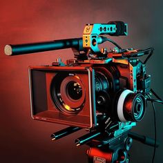 a red and blue video camera on a tripod with an orange light in the background