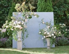 two vases filled with flowers sitting on top of a grass covered field next to bushes