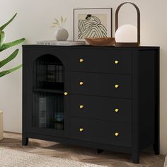 a black cabinet with gold knobs in a room next to a potted plant