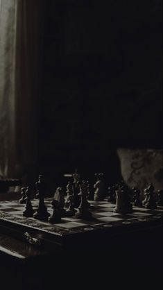 a black and white photo of chess pieces on a table in front of a window