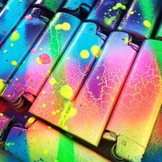 many different colored lighters lined up next to each other on a table with paint splatters all over them