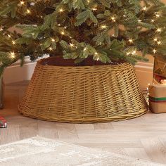 a small christmas tree in a wicker basket with lights on the top and presents under it