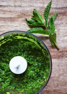 a food processor filled with green pesto and topped with a white candle next to fresh mint leaves