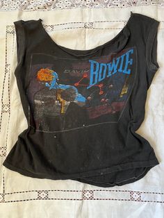 1980s Original 1983 David Bowie Concert Let's Dance / Serious Moonlight Tour Bootleg Pop Rock Band Tee Shirt Single Stitch RARE Size On Tag: no tag Modern Size: M Measurements in inches, laid flat: (Double for circumference) Pit to Pit 19 Waist 18 Hip/bottom edge 19 Length shoulder to bottom 21   No tag but feels like 50/50 Cotton Poly All vintage items have been given estimated ages based on quality, materials, design and features of the pieces. These are estimates and not exact.  All items are in wearable vintage condition, unless otherwise stated. We do our best to show any major issues like rips or discoloration in photos of the item.  Measurements are taken by hand. David Bowie T Shirt Vintage, Bowie Shirt Outfit, Vintage Crew Neck Tops For Music Festival, Vintage Cotton Top For Music Festival, Cotton Vintage Top For Music Festival, Vintage Black Top For Music Festival, Black Vintage Print 90s Style Top, 90s Graphic Print Festival Tops, Vintage Print Tops For Concert