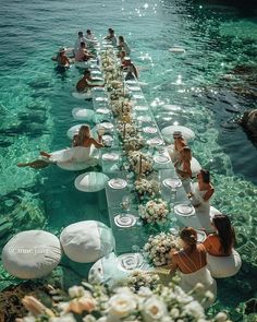 a long table is set up in the water with white flowers and plates on it