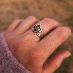 a woman's hand with a flower ring on top of her finger, in front of a field