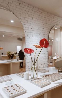 a table with flowers and jewelry on it in front of a mirror that is reflecting the room