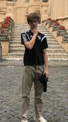 a young man standing in front of some steps with his hand to his mouth and looking at the camera