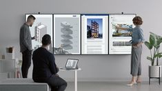 three people are standing in front of two large screens with architectural drawings on them and one man is pointing at the screen