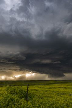 a field with green grass and storm clouds