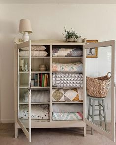 a white cabinet filled with lots of pillows and blankets next to a wall mounted mirror