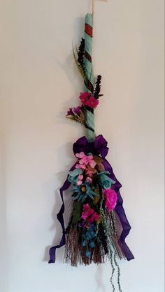 a wall hanging decoration with flowers and ribbons on it's side, next to a candle