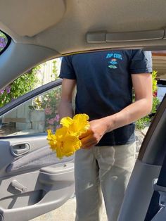 a man is holding a yellow flower in his hand while standing next to a car