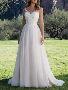 a woman in a wedding dress standing on the grass with mountains in the back ground