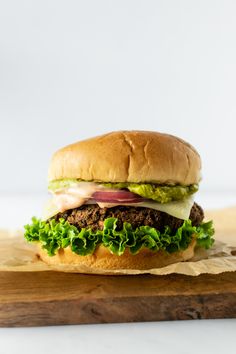 a hamburger with lettuce, tomato and onion on a wooden cutting board next to a white background