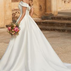 a woman in a white wedding dress holding a bouquet and posing for the camera with her back to the camera