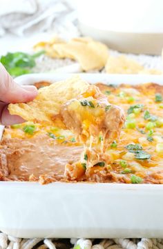 a hand dipping a tortilla chip into a casserole dish