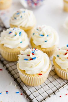 cupcakes with white frosting and sprinkles on a cooling rack