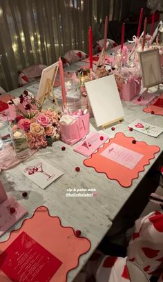 the table is set up with pink and red flowers, cards, candles, and other items