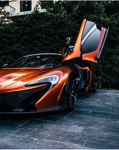 an orange and black sports car parked in front of a building with its doors open