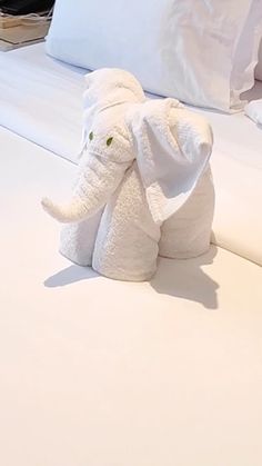 an elephant stuffed animal sitting on top of a bed next to white sheets and pillows