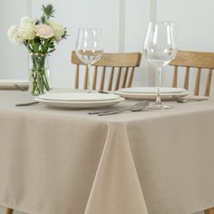 the table is set for two with white plates and silverware on it, along with flowers in vases