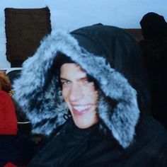 a person wearing a furry hood and smiling at the camera with other people in the background