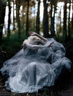 a woman in a white dress is laying on the ground surrounded by trees and grass