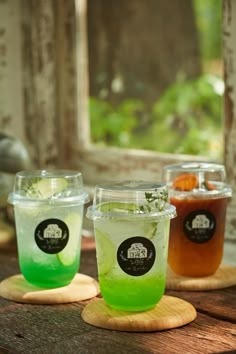 three different colored drinks sitting on top of wooden coasters