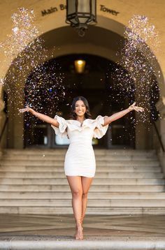 a woman in a white dress standing on steps with her arms spread out and confetti falling from the air