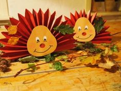 two red hedgehogs sitting on top of a wooden table next to autumn leaves