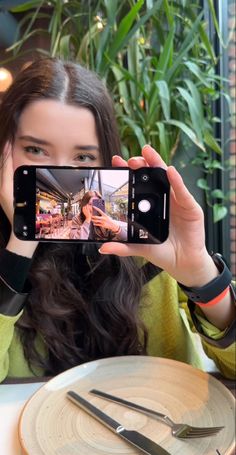 a woman taking a selfie with her cell phone at a table in a restaurant