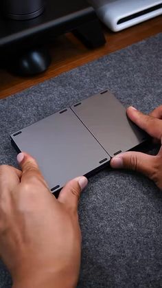 two hands holding an electronic device on top of a carpeted floor next to a laptop computer