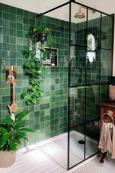 a bathroom with green tiles and a plant in the corner, next to a shower stall