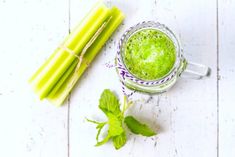 a glass mug filled with green liquid next to some celery sticks and leaves