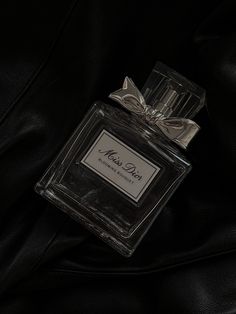 a bottle of perfume sitting on top of a black leather jacket with a bow around it's neck