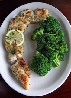 a white plate topped with chicken and broccoli next to a slice of lemon