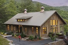 a house with a metal roof surrounded by trees and mountains in the background at dusk