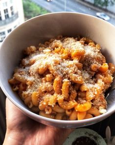 a person holding a bowl of pasta in front of a cityscape view window