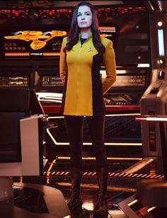 a woman in yellow and black outfit standing next to a tv screen with the words star trek written on it