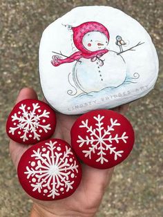 three red and white painted rocks with snowflakes on them in front of a rock