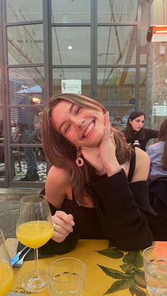 a woman sitting at a table with drinks in front of her and smiling for the camera