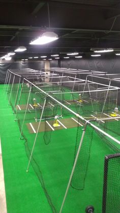 an indoor batting cage with lights on the ceiling and green grass in front of it