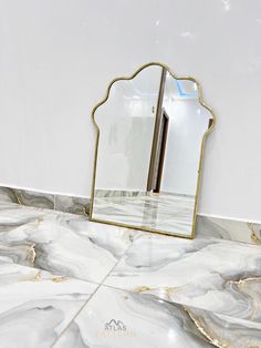 a mirror sitting on top of a marble counter next to a white wall with gold trim