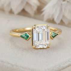 an emerald and diamond engagement ring on a white cloth with feathers in the back ground